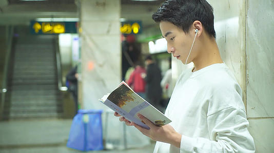 男青年在地铁站着看书视频的预览图