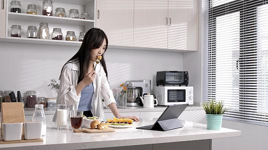 女性在厨房吃水果看电脑视频的预览图