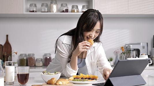 女性在厨房吃面包看电脑移镜视频的预览图
