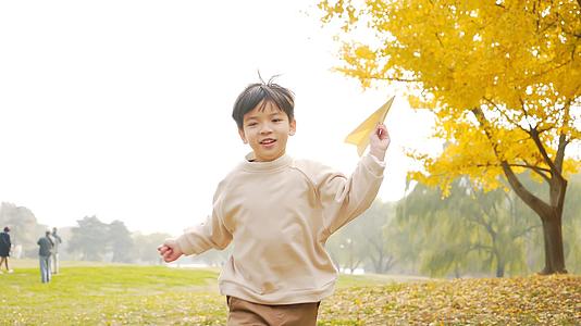 4K秋季公园草地上扔纸飞机的小男孩视频的预览图
