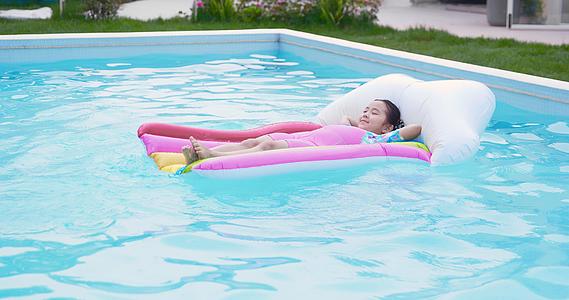 8K夏日可爱小女孩躺在泳池里的漂浮床上视频的预览图