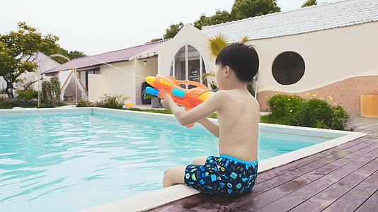 小男孩坐在泳池边玩水枪视频的预览图