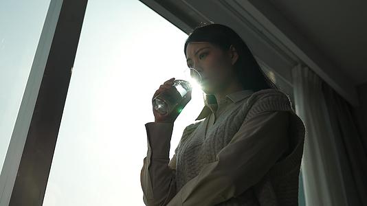 站在窗前拿水杯的抑郁女青年视频的预览图