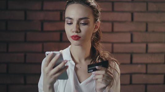 年轻女性使用手机和银行卡在砖房网上购物视频的预览图
