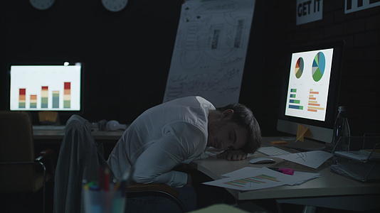 疲惫的商人睡在黑暗的办公室工作台前的电脑上视频的预览图