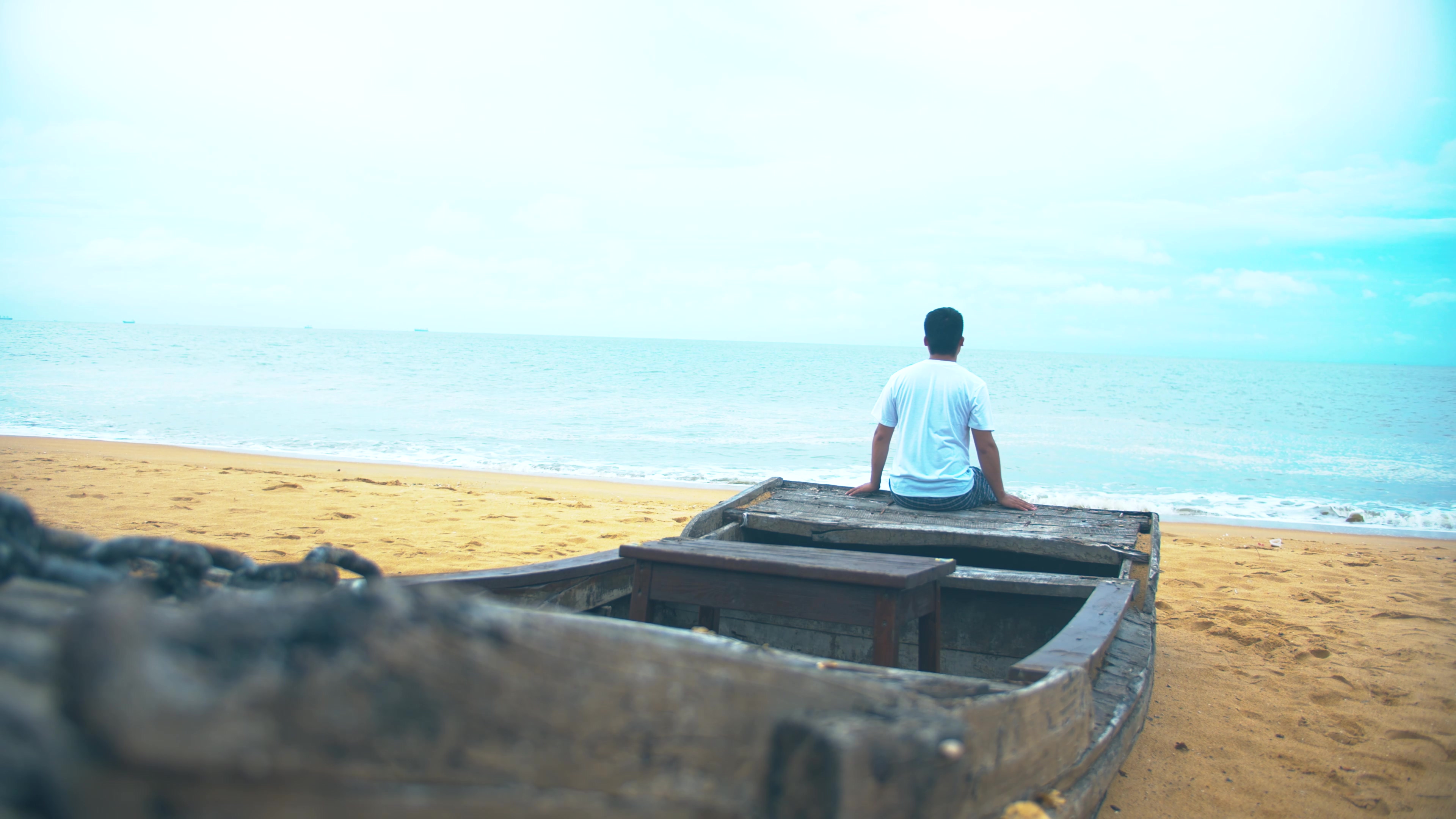 4K实拍沙滩上男人孤独坐在木船上视频素材视频的预览图