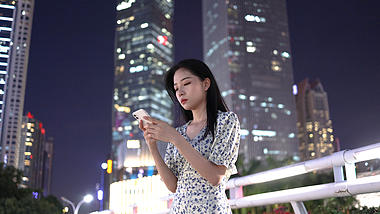 4k都市夜晚在高楼大厦下玩手机的年轻美女视频的预览图